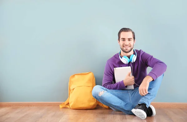 Estudiante con tableta sentado en el suelo contra la pared de color —  Fotos de Stock