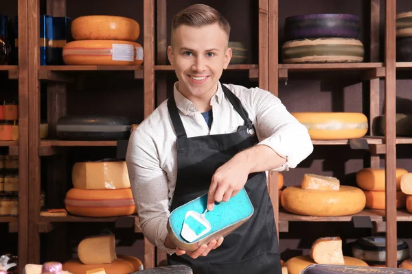 Young worker slicing cheese in shop