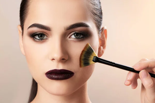 Professional visage artist applying makeup on woman's face against light background — Stock Photo, Image