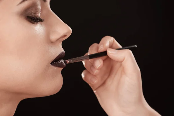 Professional visage artist applying makeup on woman\'s face against black background