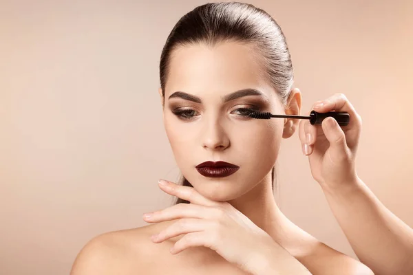 Professional visage artist applying makeup on woman's face against light background — Stock Photo, Image