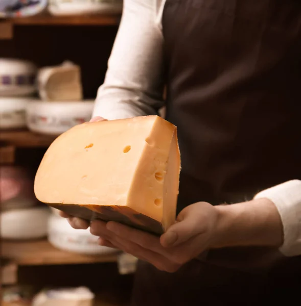 Young worker holding cheese in shop