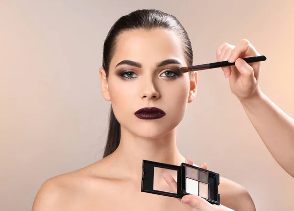 Professionell visage konstnären tillämpa makeup på kvinnans ansikte mot ljus bakgrund — Stockfoto