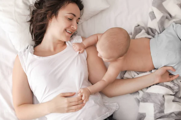 Joven madre y su bebé tumbados en la cama en casa — Foto de Stock