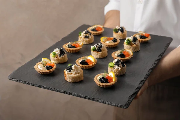 Hombre sosteniendo plato de pizarra con aperitivos de caviar sobre fondo claro —  Fotos de Stock