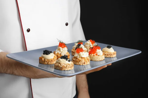 Man håller plattan med kaviar aptitretare på svart bakgrund — Stockfoto