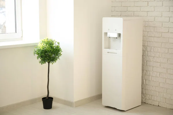 Modern water cooler and plant near brick wall