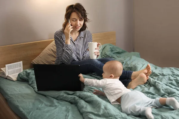 Ibu muda dengan bayi bekerja di tempat tidur di rumah — Stok Foto