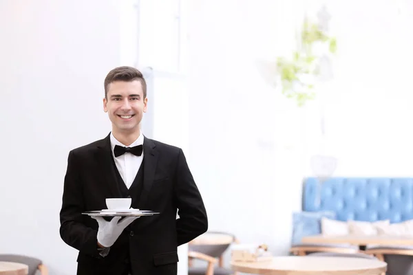 Привабливий молодий офіціант тримає піднос з чашкою кави в приміщенні — стокове фото