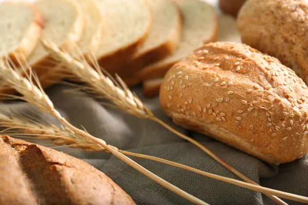 Tasty bun and wheat spikes on table. Freshly baked bread products — Stock Photo, Image