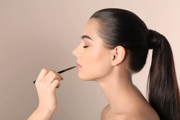 Artista de visage profesional aplicando maquillaje en la cara de la mujer contra el fondo claro — Foto de Stock