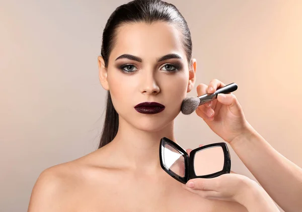 Artista de visage profesional aplicando maquillaje en la cara de la mujer contra el fondo claro — Foto de Stock