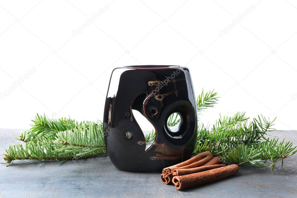 Aroma lamp with fir tree twigs and cinnamon sticks on table against white background