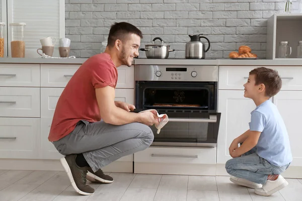 Kleine jongen zijn vader bak koekjes in de oven binnen kijken — Stockfoto