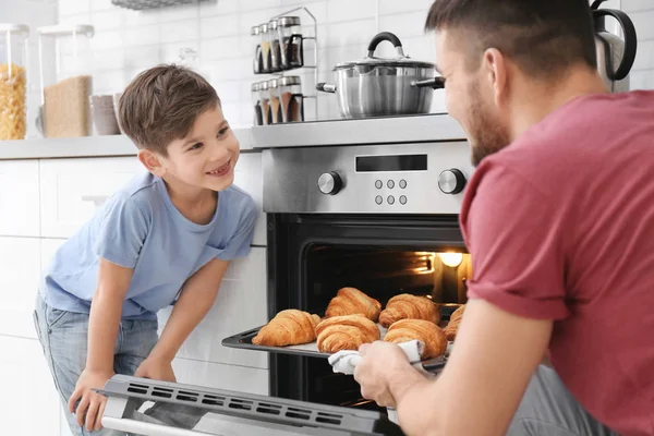 Liten pojke tittar på hans far baka croissanter i ugn inomhus — Stockfoto