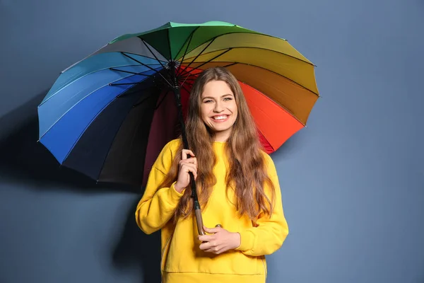 Young woman with rainbow umbrella on color background