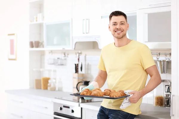 Hombre sosteniendo bandeja para hornear con deliciosos croissants caseros en la cocina — Foto de Stock