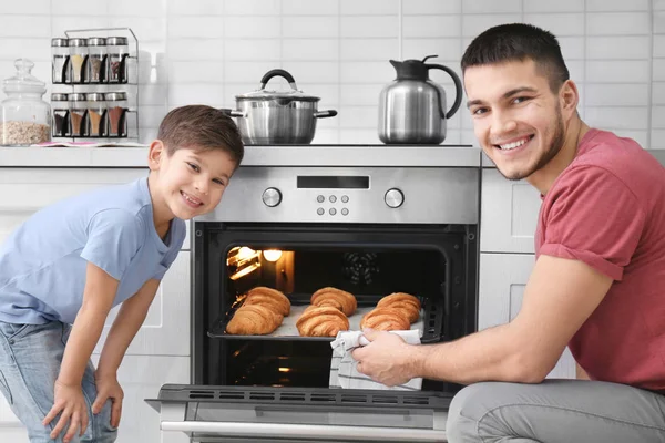 Мальчик смотрит, как его отец печет круассаны в духовке в помещении. — стоковое фото