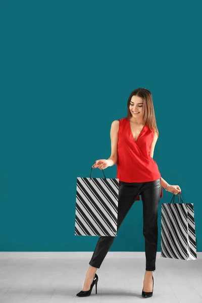 Young woman with shopping bags against color wall — Stock Photo, Image