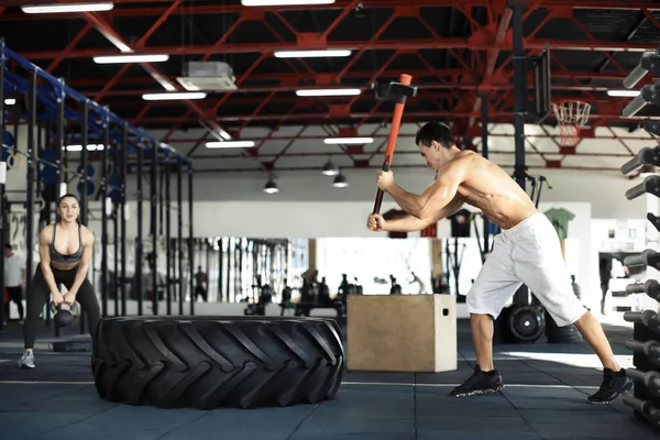 年轻肌肉男子打重轮胎锤在健身房 — 图库照片