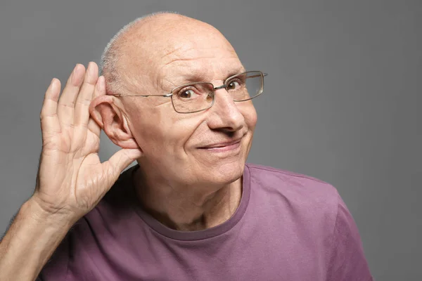 Homem idoso com problema auditivo em fundo cinza — Fotografia de Stock