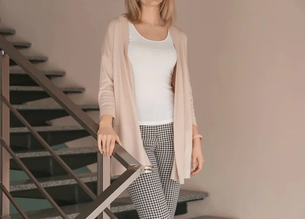 Young woman in stylish cardigan on stairs indoors — Stock Photo, Image