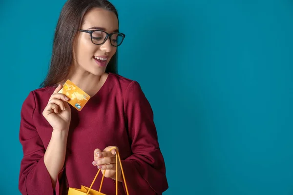 Belle jeune femme avec sac à provisions et carte de crédit sur fond de couleur — Photo