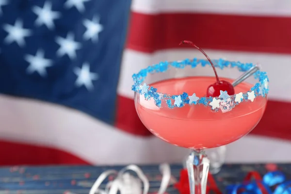 Glass with alcohol cocktail on table against American flag — Stock Photo, Image
