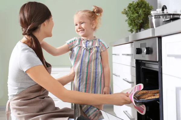 小女孩看她的母亲在烤箱烘烤饼干在室内 — 图库照片