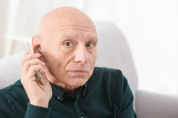 Homem sênior com aparelho auditivo falando no telefone dentro de casa — Fotografia de Stock