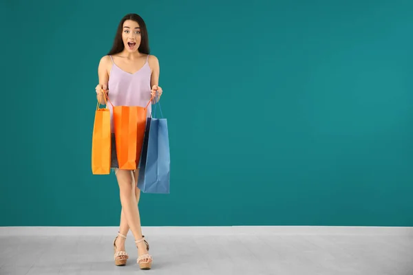Surprised young woman with shopping bags against color wall — Stock Photo, Image
