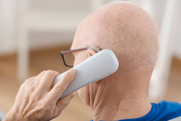 Старший мужчина со слуховым аппаратом разговаривает по телефону в помещении — стоковое фото