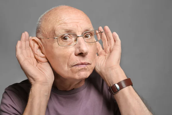 Älterer Mann mit Hörproblemen auf grauem Hintergrund — Stockfoto