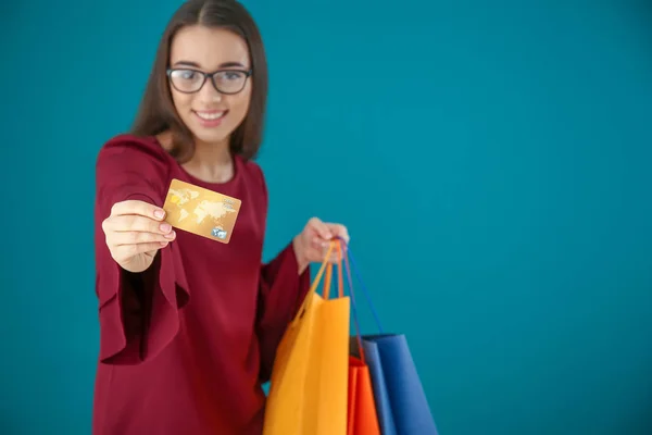 Bella giovane donna con borse della spesa e carta di credito su sfondo a colori — Foto Stock