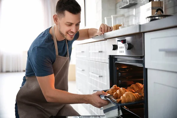 Man tar bakplåt med läckra croissanter av elektrisk ugn i kök — Stockfoto