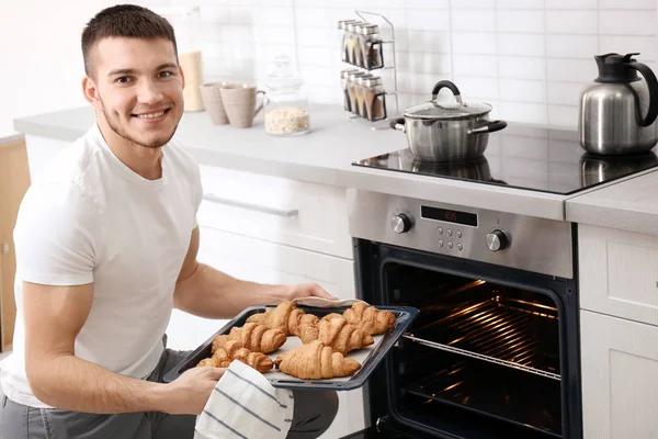 Young man baking croissants in oven indoors