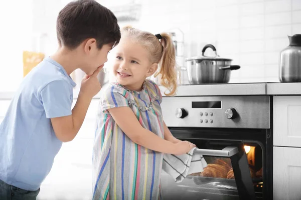 Weinig kinderen sluipen croissants uit oven binnenshuis — Stockfoto