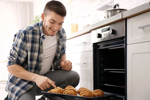 Young man baking croissants in oven indoors