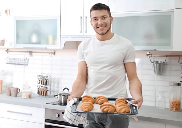 Man håller bricka med croissanter i köket. Färskt från ugnen — Stockfoto