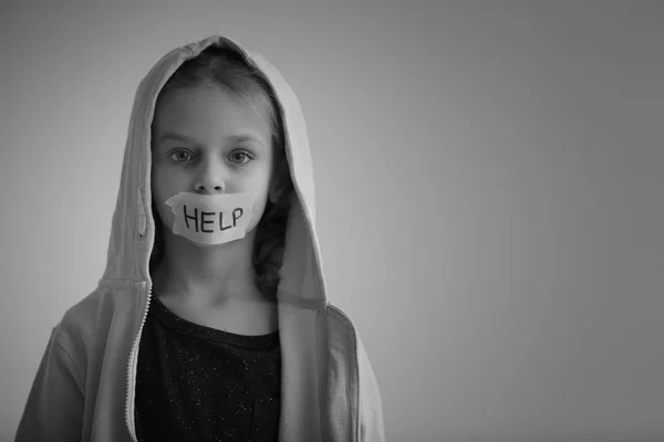 Sad little girl with taped mouth and word "Help" on grey background, black and white effect — Stock Photo, Image