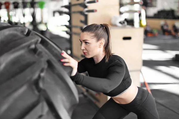 Mladý svalnatý žena překlápění těžké pneumatiky v tělocvičně — Stock fotografie