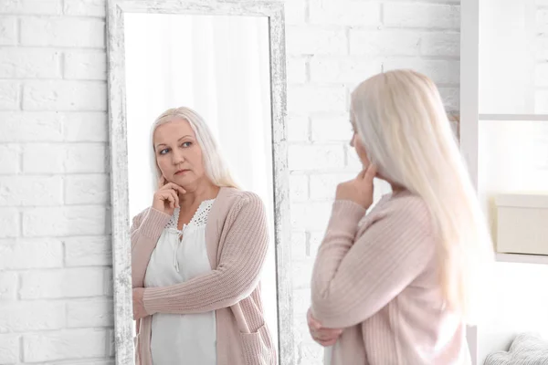 Femme mûre réfléchie debout près du miroir à la maison — Photo