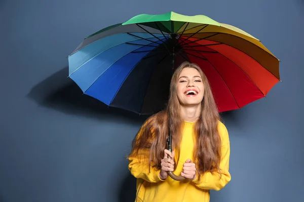 Young woman with rainbow umbrella on color background — Stock Photo, Image