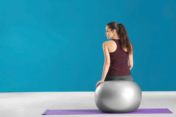 Mooie sportieve vrouw zittend op fitball tegen kleur muur — Stockfoto