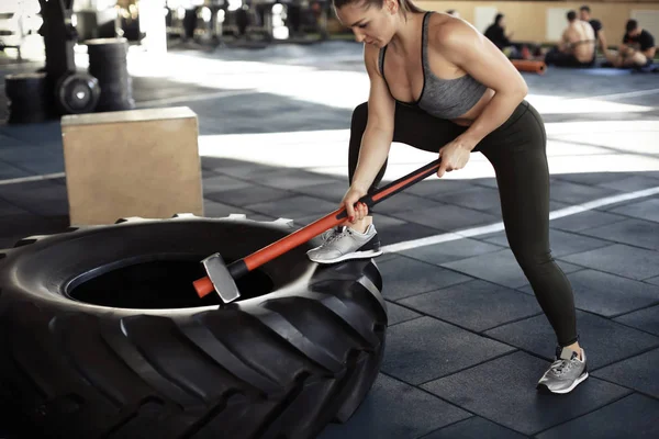 Mujer muscular joven golpeando neumático pesado con martillo en el gimnasio — Foto de Stock