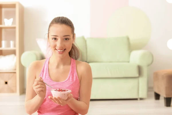 Спортивная молодая женщина ест йогурт с ягодами после тренировки дома — стоковое фото