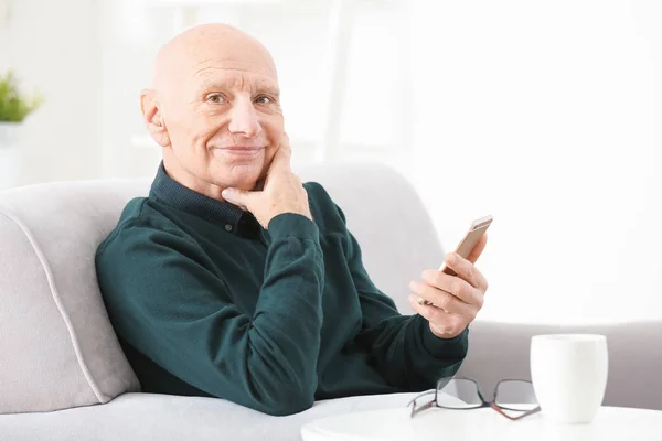 Senior man met gehoorapparaat gebruikend smartphone binnenshuis — Stockfoto