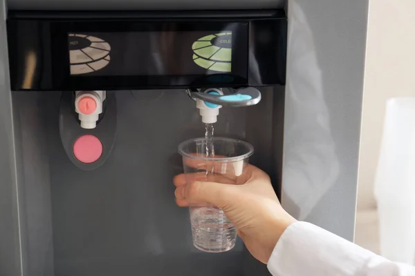 Mulher que enche o copo plástico do refrigerador de água, close-up — Fotografia de Stock