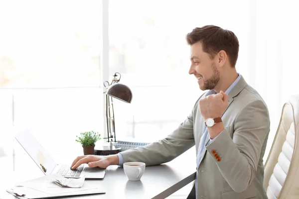 Счастливый бизнесмен с ноутбуком работает за столом в офисе — стоковое фото