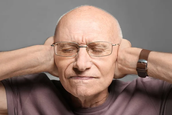 Äldre man som täcker öronen på grå bakgrund. Hörselskada — Stockfoto